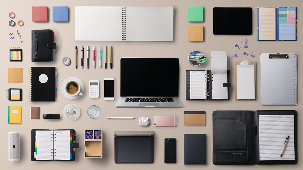 Office supplies neatly arranged on a table, including a laptop, notebooks, pens, and a smartphone.