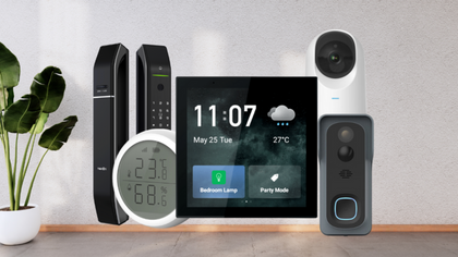 Smart home devices on a wooden surface, including a screen, camera, thermometer, and plant.