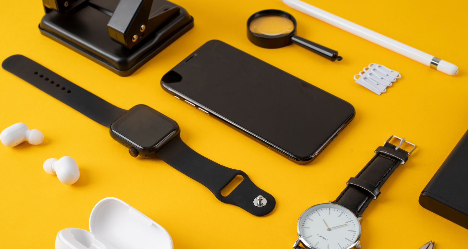 Smartphone, black smartwatches, wireless earbuds, magnifier, and a white watch on yellow background.
