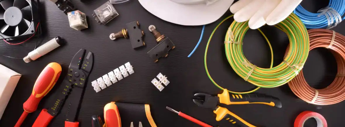 Electrical tools and supplies on a black surface, including wires, pliers, and gloves.