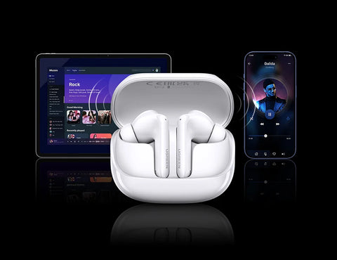 White wireless earbuds in an open case, with a tablet and smartphone in the background.