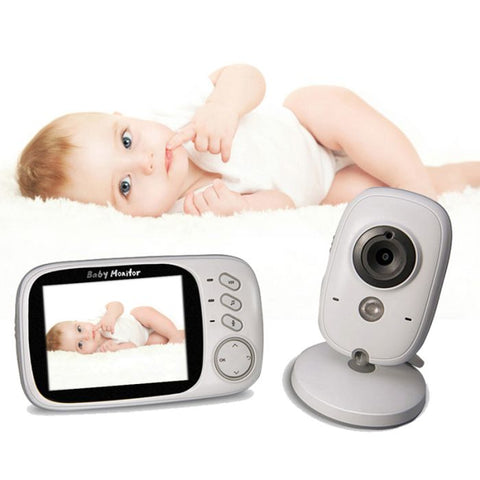 Baby in white outfit on soft surface; baby monitor shows same image; gray and white camera nearby.